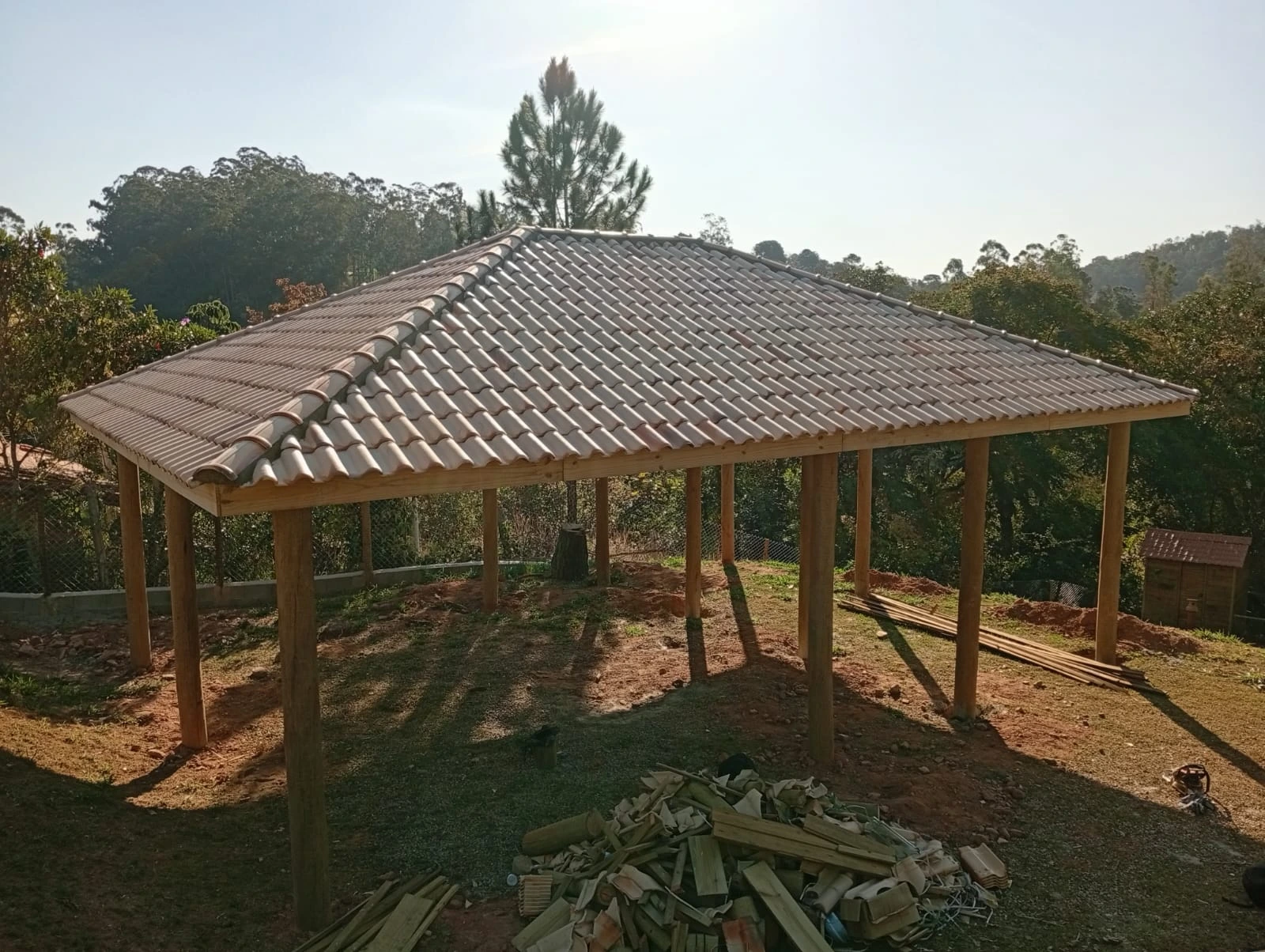 Foto com vista de cima de uma estrutura com telhado de telha cerâmica. Estrutura feita de eucalipto tratado